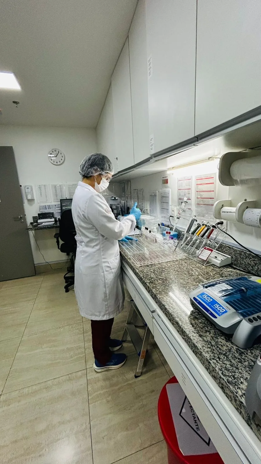 Andrya Silva em bancada de laboratório hospitalar, coletando dados para análise ergonômica do posto de trabalho.