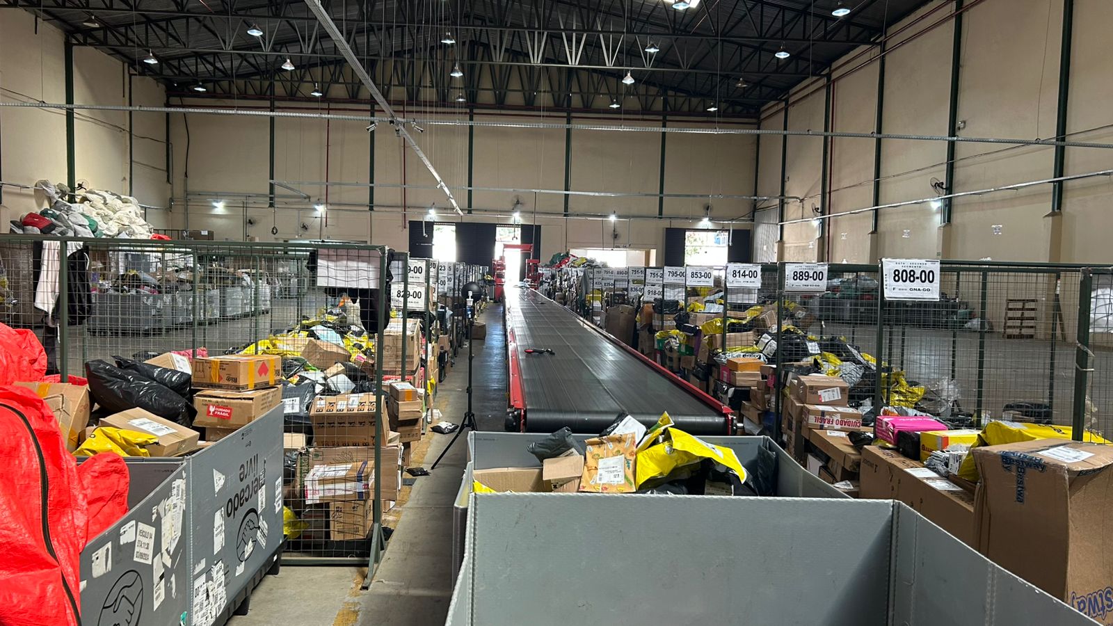 Vista interna de galpão de logística com esteira de triagem e boxes de separação de encomendas, ambiente avaliado quanto à exposição ao calor.