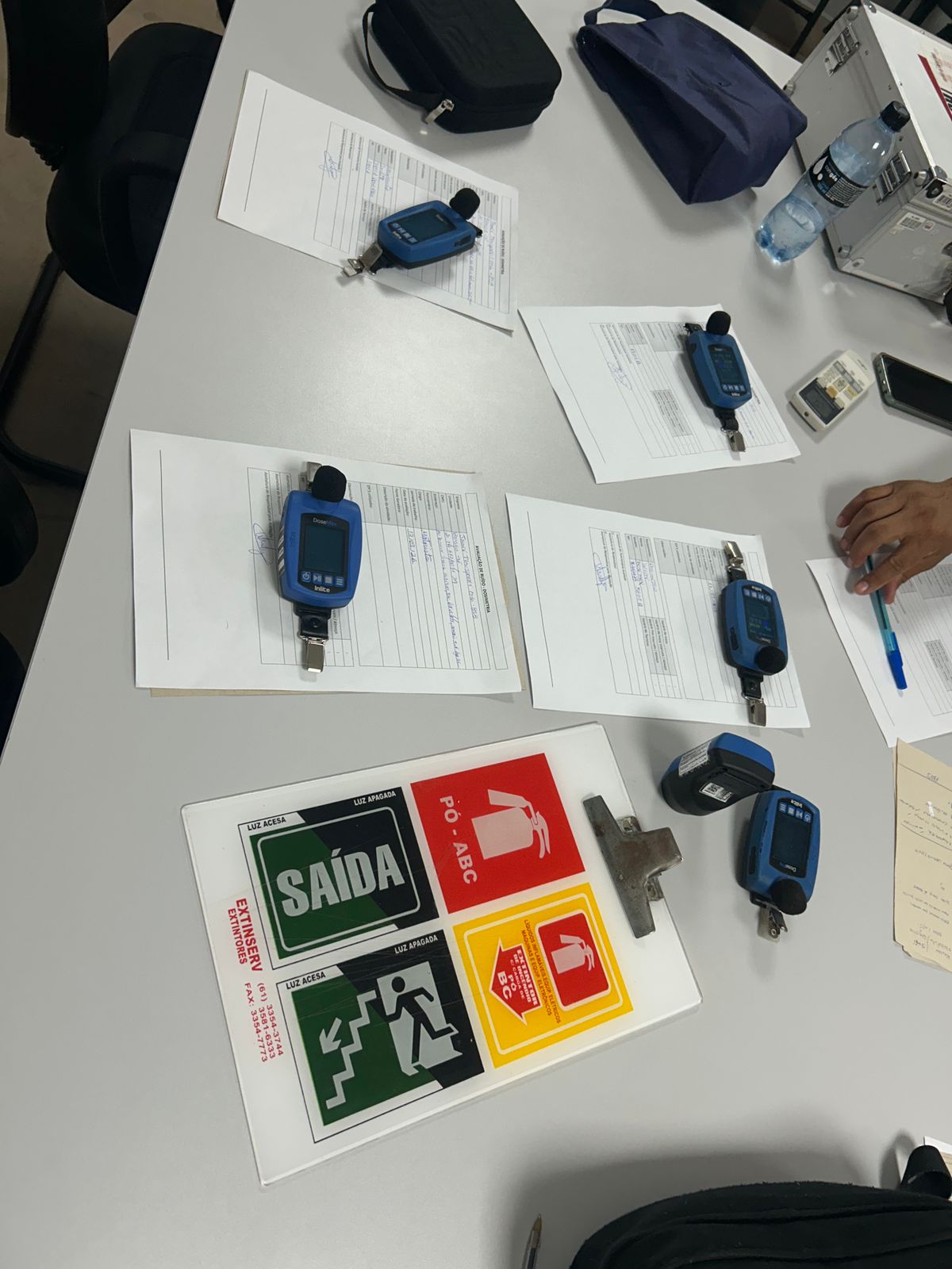 Dosímetros de ruído posicionados sobre formulários de avaliação, equipamentos utilizados em dosimetria e avaliação de vibração.